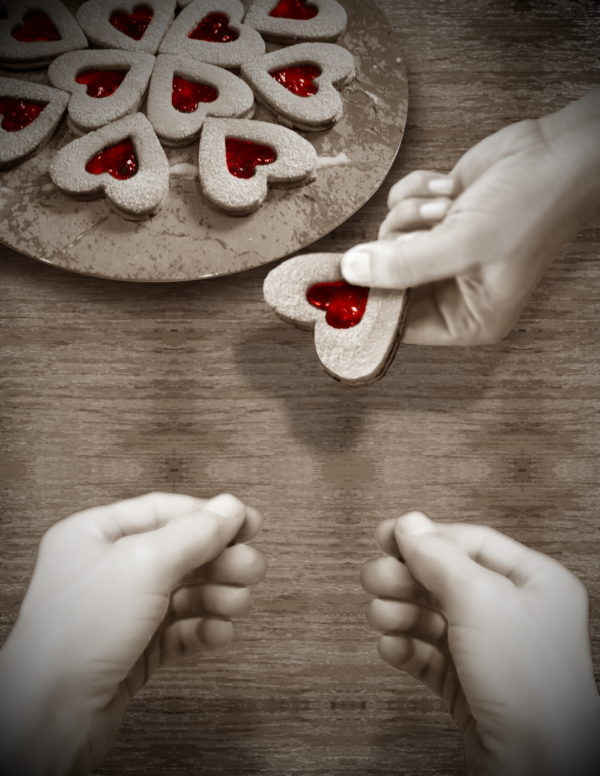 One hand holds a heart-shaped cookie over the table. Two hands are about to sign "more."